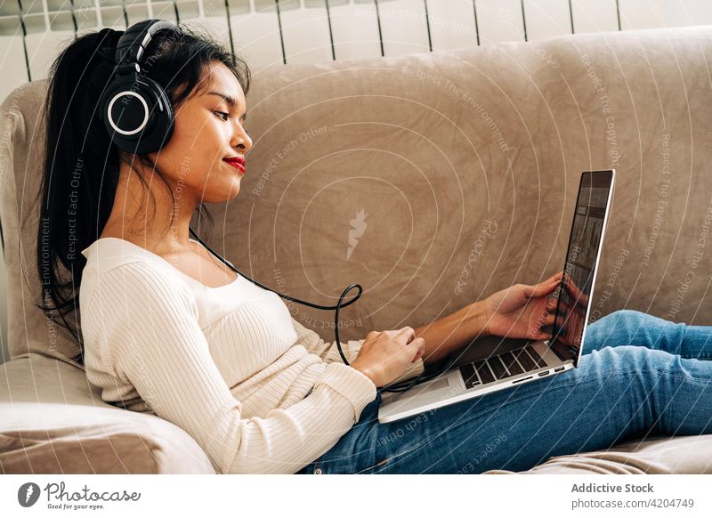 Verträumte Frau mit Laptop und Kopfhörern Sofa online Internet benutzend Surfen zuschauen Pause Browsen Apparatur Anschluss Netbook Liege Arbeit Kälte