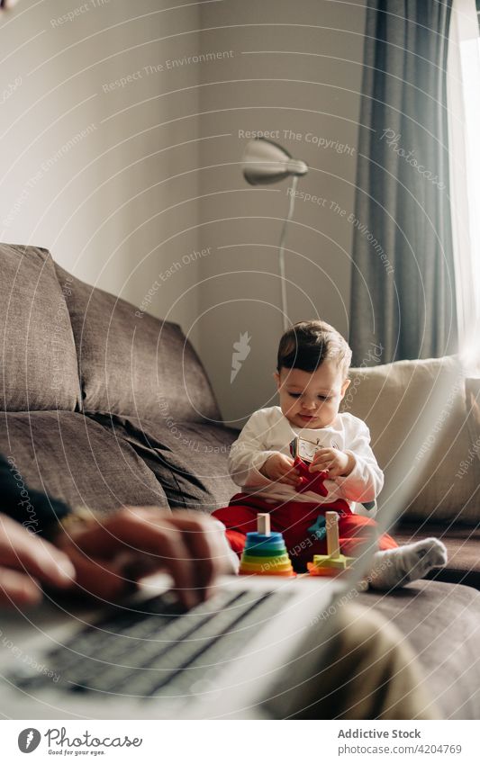 Neugieriges Baby spielt mit Spielzeug auf der Couch in der Nähe von anonymen Vater mit Laptop spielen Sofa Zapfen Turm Tippen Zusammensein spielerisch neugierig