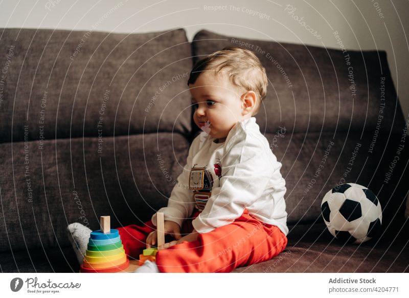 Neugieriges Baby spielt mit Spielzeug auf der Couch spielen Sofa Zapfen Turm spielerisch neugierig farbenfroh hölzern Kleinkind Junge Kind niedlich Kindheit