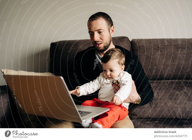 Junger Vater mit kleinem Sohn schaut Video auf Netbook Mann Kind zuschauen Karikatur Laptop Zusammensein Liebe Sofa Partnerschaft heimwärts online Bonden jung