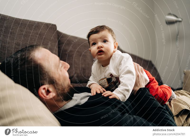 Glücklicher Mann liegt auf dem Sofa und spielt mit seinem kleinen Sohn Baby Lügen Liege spielen Zusammensein Liebe Partnerschaft positiv Umarmung Vater