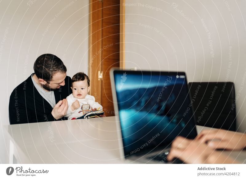 Vater und Baby lesen ein Buch in der Nähe der Mutter, die am Laptop arbeitet Familie Arbeit freiberuflich Browsen Kinderbetreuung Elternschaft Entwicklung