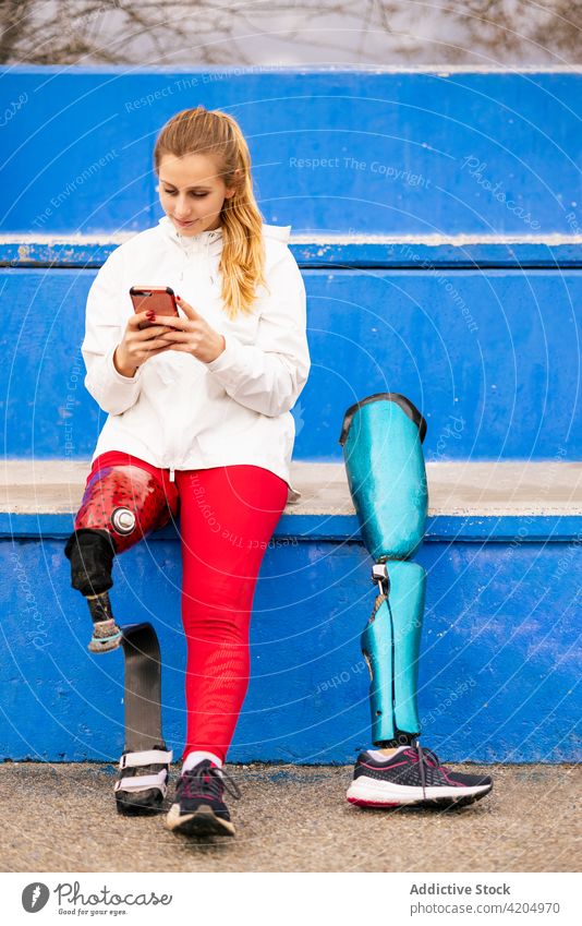 Sportlerin mit bionischer Prothese nutzt Smartphone im Stadion Browsen Bein Prothesen Athlet Bionik Training Pause Frau paralympisch künstlich Glied