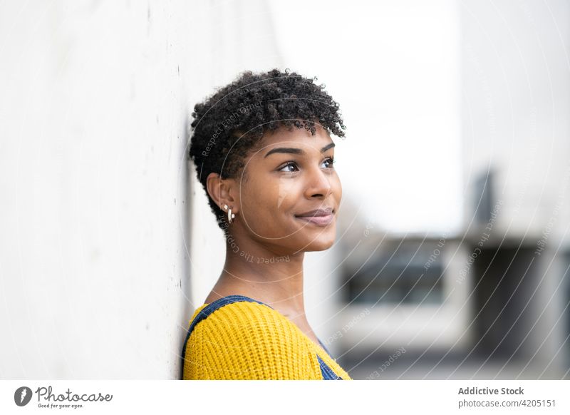Erfreute ethnische Frau auf der Straße und schaut weg Lächeln Afro-Look Frisur Großstadt urban gesamt Outfit heiter schwarz Afroamerikaner Wand fettarm positiv