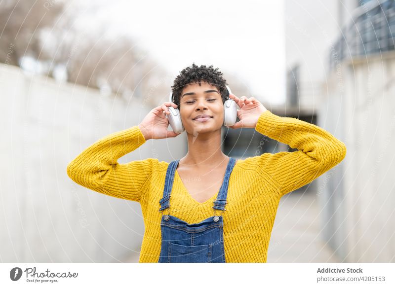 Glückliche schwarze Frau, die mit Kopfhörern in der Stadt Musik hört zuhören verträumt genießen Gesang Drahtlos sorgenfrei Großstadt ethnisch Afroamerikaner