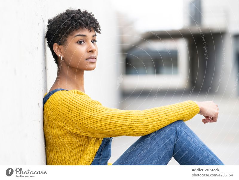Erfreute ethnische Frau auf der Straße und schaut weg Lächeln Afro-Look Frisur Großstadt urban gesamt Outfit heiter schwarz Afroamerikaner Wand fettarm positiv