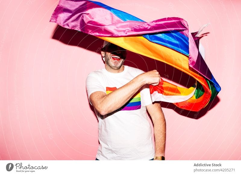 Glücklicher Mann mit Make-up winkt LGBT-Flagge in rosa Studio Homosexualität lgbt Fahne heiter schwul Lächeln Konzept Stolz Regenbogen gleich männlich unrasiert