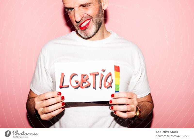 Positive Homosexuell zeigt Papier mit LGBTIQ Aufschrift in rosa Studio Mann Homosexualität schwul Stolz queer lgbt Grimasse Konzept manifestieren abstützen