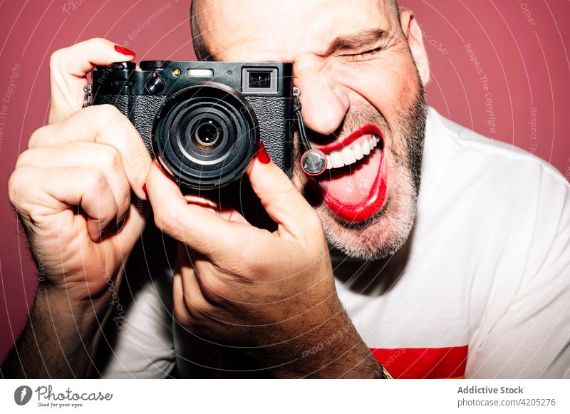 Fröhlicher Kerl mit Make-up, der mit geöffnetem Mund ein Foto in die Kamera hält Mann fotografieren Homosexualität schwul Fotograf expressiv Mund geöffnet Bild