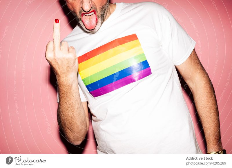 Anonymer homosexueller Mann mit Make-up und Bart zeigt Mittelfinger ficken lgbt schwul ausspannen auflehnen Stolz Fahne Konzept unanständig Freiheit Regenbogen