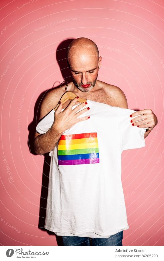 Exzentrischer Mann mit Make-up zeigt T-Shirt mit Regenbogenflagge in rosa Studio lgbt Fahne Homosexualität schwul exzentrisch Stolz Konzept Stil gleich Toleranz
