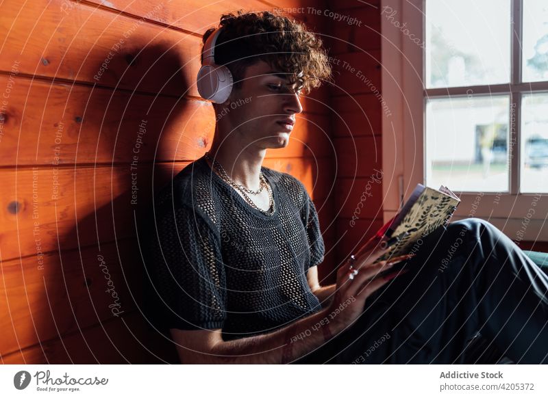 Queer mit Headset, der in einer Hütte ein Notebook liest schwul lesen Kopfhörer zuhören Gesang Freizeit Chalet Porträt benutzend Gerät Mann queer freie Zeit