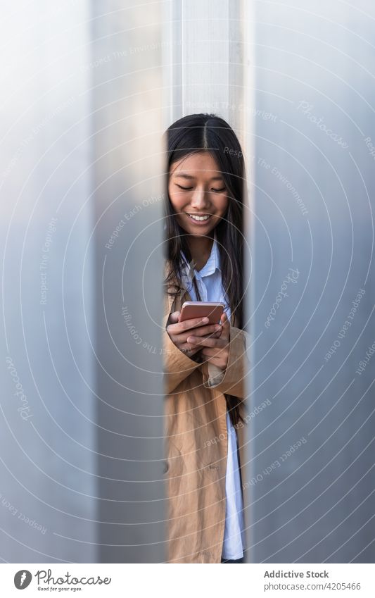 Fröhliche ethnische Frau, die eine SMS auf ihrem Smartphone schreibt benutzend Nachricht heiter Straße Browsen Internet online Surfen asiatisch Glück Apparatur