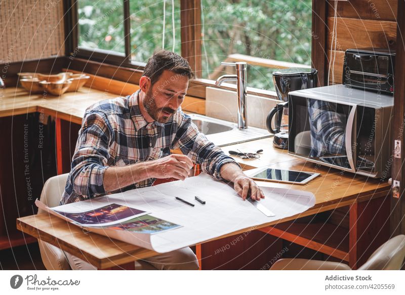 Beschäftigter Mann zeichnet Entwurf eines Hauses zu Hause Architekt zeichnen Bauplan Skizze Projekt Gebäude beschäftigt Papier männlich Plan heimwärts sitzen