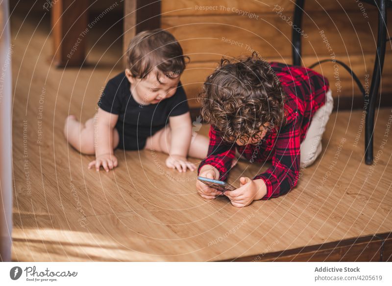 Niedliche Geschwister sitzen auf dem Holzboden im Haus Kinder Geschwisterkind Browsen Smartphone wenig niedlich heimwärts unterhalten Stock bezaubernd Junge