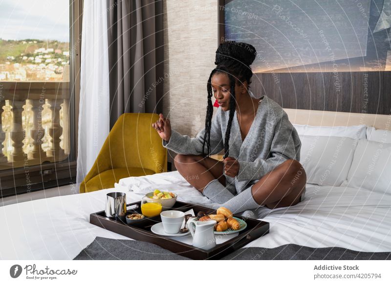 Glückliche junge schwarze Dame beim Frühstück in einem gemütlichen Hotelzimmer Frau trinken Kaffee Bett Inhalt Lächeln Komfort Tourist sich[Akk] entspannen