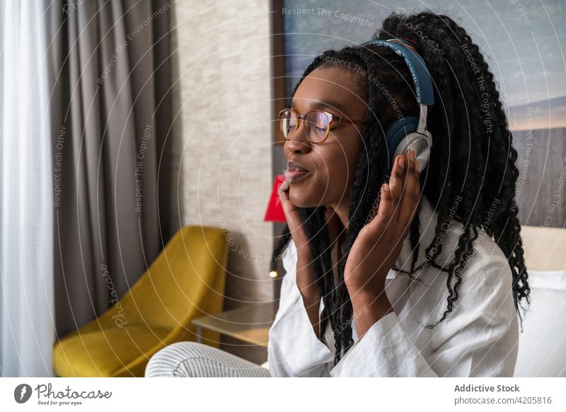Lächelnde junge schwarze Frau, die ein Mobiltelefon benutzt und mit Kopfhörern Musik hört online positiv Internet Anschluss Kommunizieren Smartphone