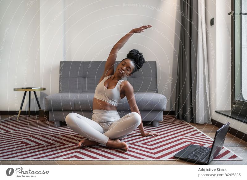 Fit ethnischen Dame Stretching Beine während der Durchführung Yoga-Pose während Online-Training Frau Laptop Video Tutorial online Achtsamkeit Stressabbau