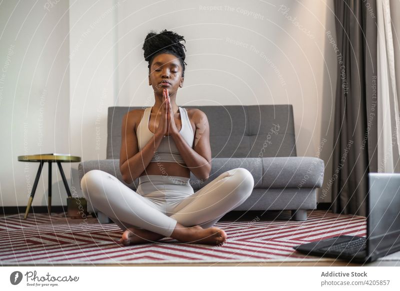 Barfüßige schwarze Frau meditiert in Padmasana Yogastellung mit geschlossenen Augen padmasana Lotus-Pose meditieren Augen geschlossen Wellness Asana Zen Laptop