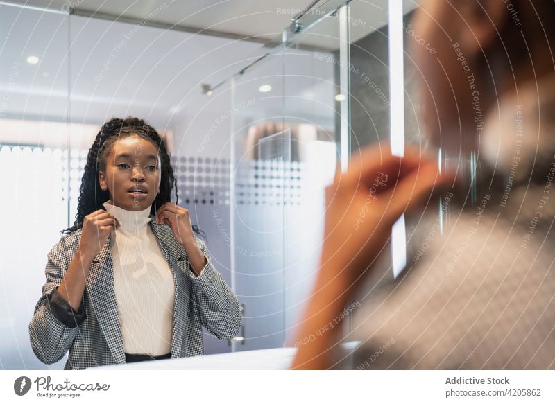Positive junge ethnische Frau lächelt beim Blick in den Spiegel im Badezimmer Lächeln selbstsicher Reflexion & Spiegelung Stil Vorschein charismatisch Glück