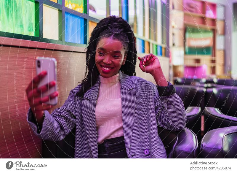 Selbstbewusste junge ethnische Frau macht ein Selfie mit ihrem Smartphone in einem Café selbstbewusst Lächeln Stil Mode Freude Optimist positiv Glück