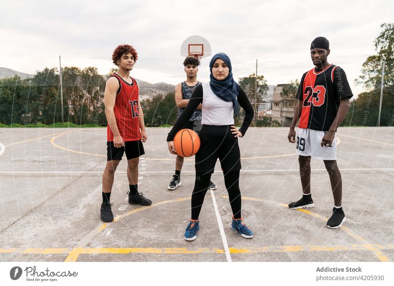 Unterschiedliche Streetball-Spieler stehen gemeinsam auf dem Basketballplatz Team Sportpark Zusammensein Bestimmen Sie Ball Straße Gericht multiethnisch