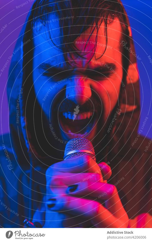 Brutaler Mann singt mit Mikrofon im Neonlicht Sänger Felsen Gesang neonfarbig Hipster laut expressiv ausführen Musik Konzert männlich Erwachsener leuchten Klang