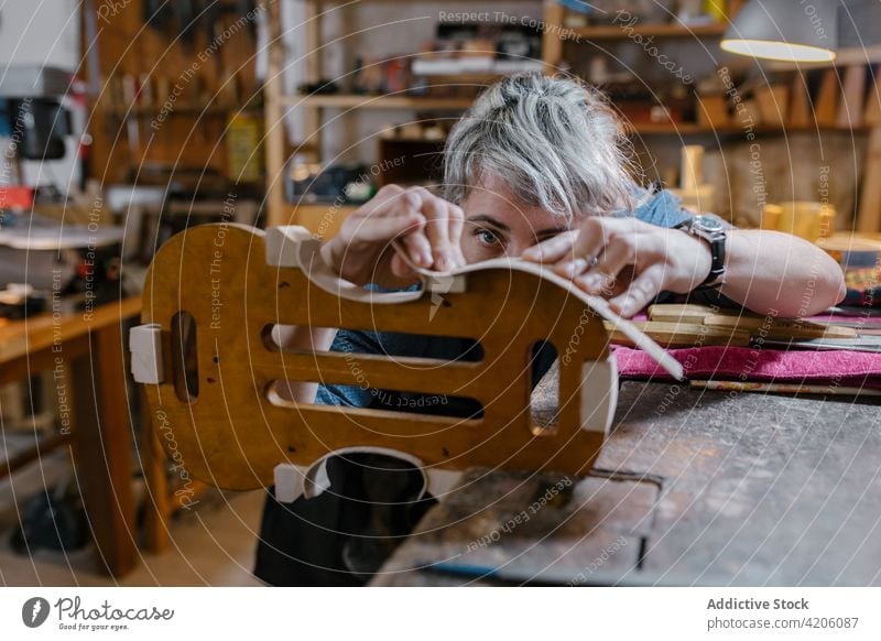 Handwerkerin beim Geigenbau in der Werkstatt schnitzen professionell Inszenierung Kurve Instrument Hobelbank Frau Kunstgewerbler Schürze Körper Lampe Arbeit