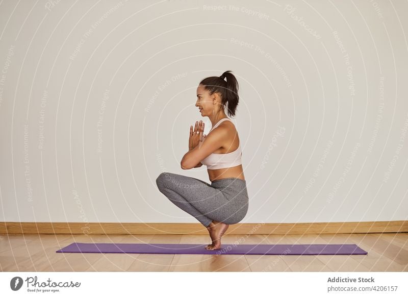 Zufriedene Frau in hockender Zehenbalance-Pose im Zimmer Namaste Yoga Hocke-Zehe-Gleichgewicht Lächeln üben Wellness Vitalität Energie Raum Inhalt froh