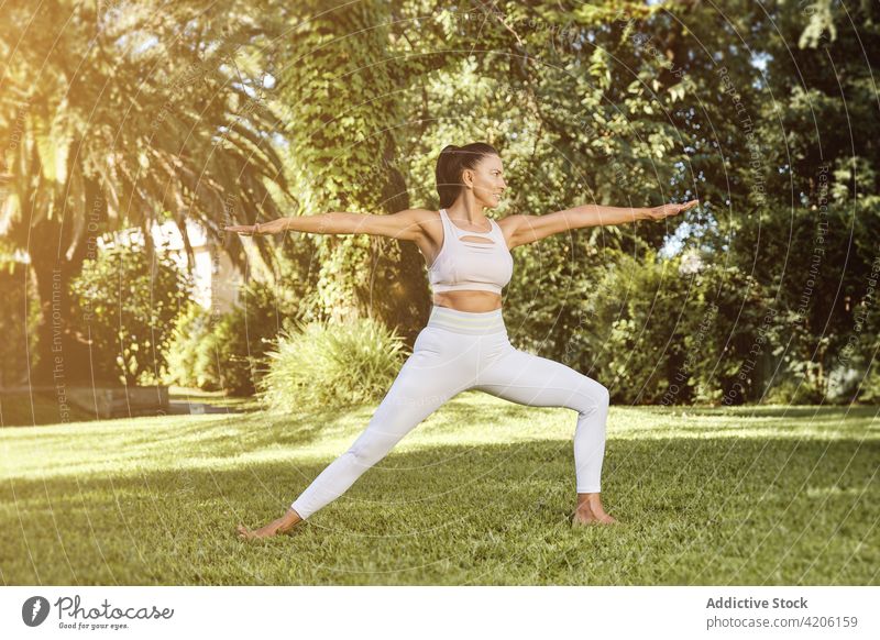Frau zeigt Warrior zwei Posen im Park Yoga Gleichgewicht Krieger zwei üben Lächeln Dehnung beweglich Wohlbefinden Glück Vitalität Gesunder Lebensstil Energie