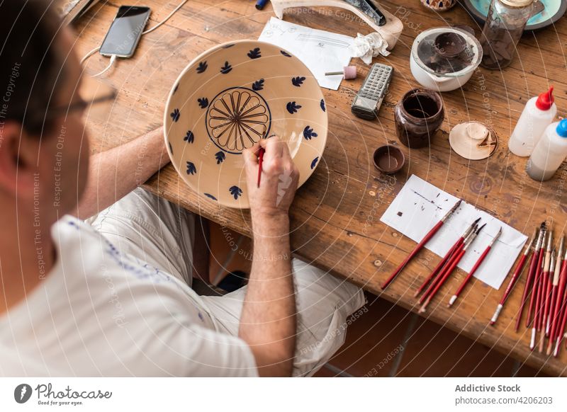 Crop Artist Zeichnung auf Keramikplatte Mann zeichnen Künstler Bürste Handwerk Kunst Werkstatt handgefertigt Hobby männlich Farbe Design Teller Talent