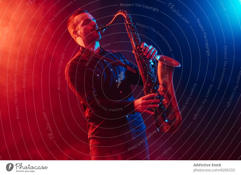 Engagierter Saxophonist spielt Saxophon im Neonlicht Mann Musiker spielen ausführen live Augen geschlossen Klang professionell Instrument Club Gesang