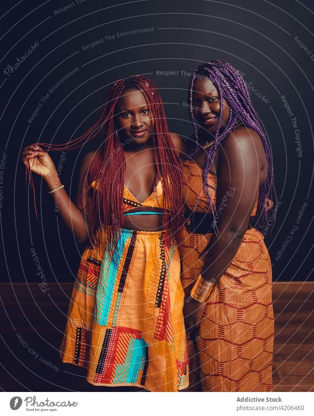 Lächelnde schwarze Frauen in traditioneller Kleidung stehen im Studio Geflecht Frisur hell Outfit Tradition Freund Atelier lange Haare Vorschein ethnisch