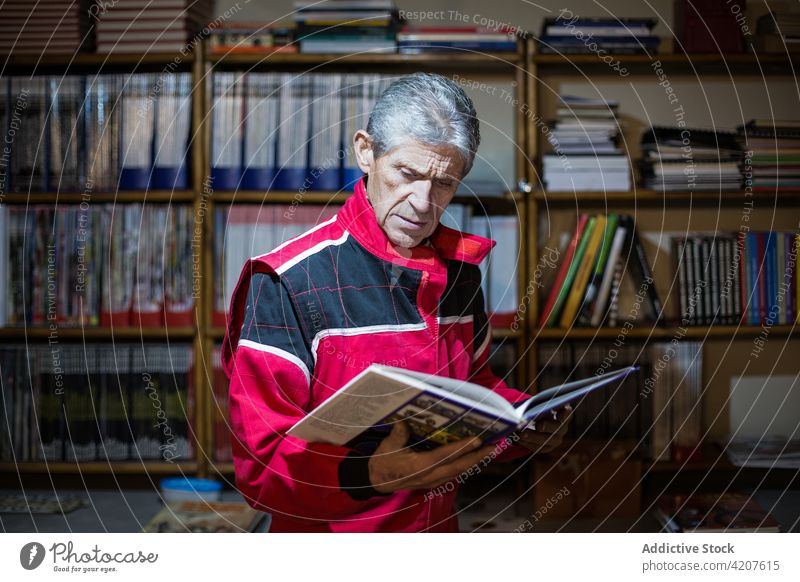 Mechaniker liest Fachliteratur in der Nähe eines Bücherregals lesen Buch professionell Techniker Literatur Wissen Lösung Mann Senior Problematik Bücherschrank