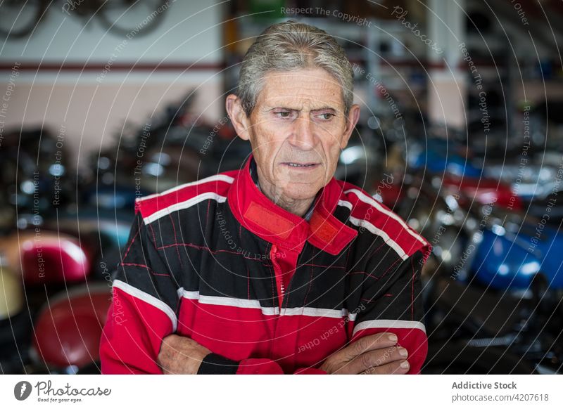 Älterer Mechaniker in professioneller Werkstatt mit beschädigten rostigen Motorrädern Arbeit Mann Reparatur Senior gealtert männlich älter Dienst