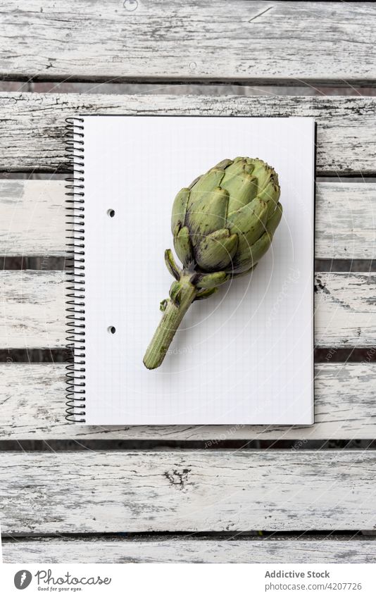 Eine Artischocke auf einem leeren Notizbuch auf dem Tisch Notebook Kraut frisch Grün Notizblock Gesundheit Lebensmittel Zweig grün Schreibtisch Papier Page