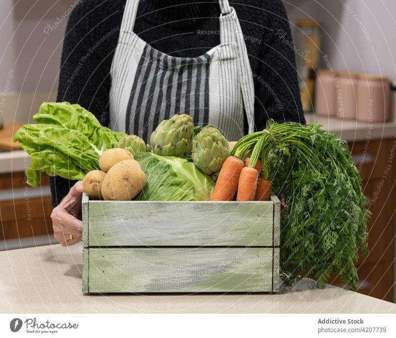 Ältere Frau mit Gemüse in Holzkiste Lebensmittelgeschäft Ernte Kasten frisch reif sortiert natürlich Senior Schürze Tisch Küche Produkt organisch hölzern
