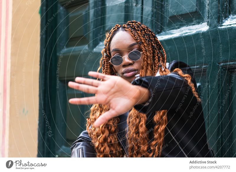Stilvolle schwarze Frau bedeckt ihr Gesicht und schaut in die Kamera cool Straße Deckblatt selbstbewusst trendy Geflecht Frisur Outfit ethnisch Afroamerikaner