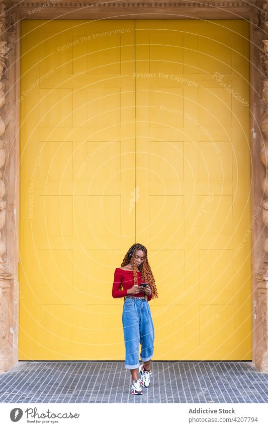 Schwarze Frau steht und hört Musik in der Nähe von großen Türen in der Stadt Großstadt Türöffnung Eingang Gebäude antik alt Straße ethnisch schwarz