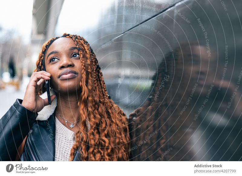 Stilvolle schwarze Frau, die auf der Straße mit ihrem Smartphone telefoniert Großstadt trendy Outfit Geflecht Frisur ethnisch Afroamerikaner Gebäude Lifestyle
