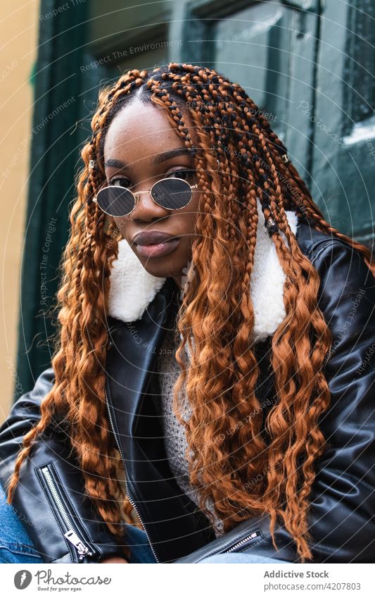 Stilvolle schwarze Frau mit Sonnenbrille schaut in die Kamera cool Straße Deckblatt selbstbewusst trendy Geflecht Frisur Outfit ethnisch Afroamerikaner urban