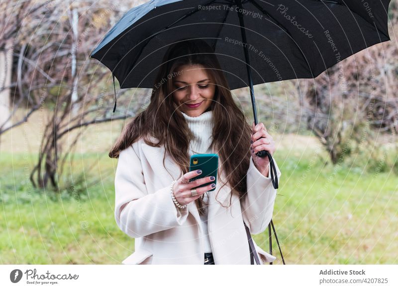 Frau mit Regenschirm und Smartphone auf der Straße benutzend Stil Telefon Mobile Frühling Mode Mantel Erwachsener Apparatur Gerät Lifestyle Browsen schlendern