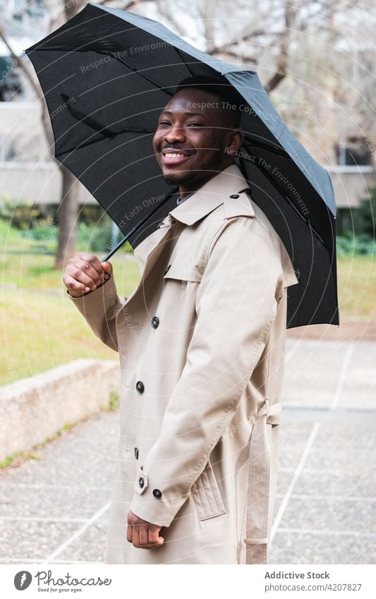 Glücklicher stilvoller schwarzer Mann mit Regenschirm Mantel Frühling Stil Lächeln Mode Wetter trendy männlich Erwachsener Afroamerikaner ethnisch urban heiter