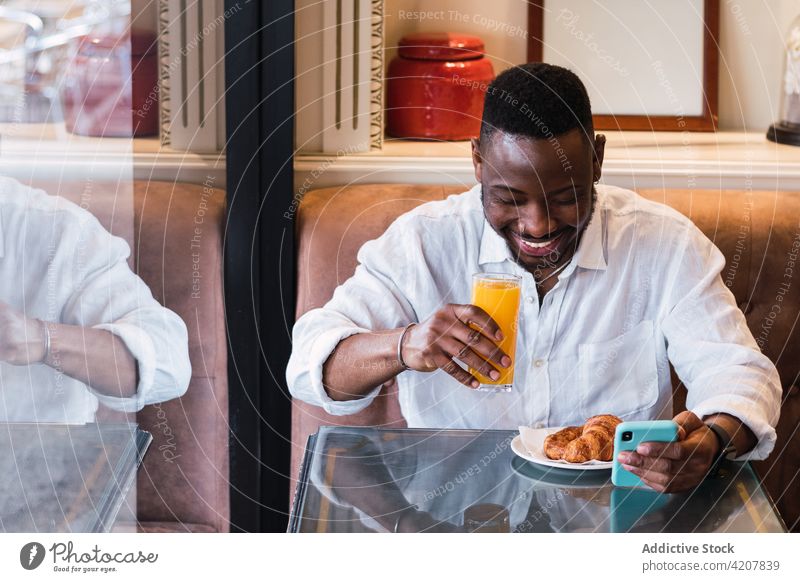 Fröhlicher schwarzer Mann mit Smartphone in einem Café benutzend Glück Telefon Mobile Saft Frühstück Browsen Erwachsener männlich Afroamerikaner ethnisch