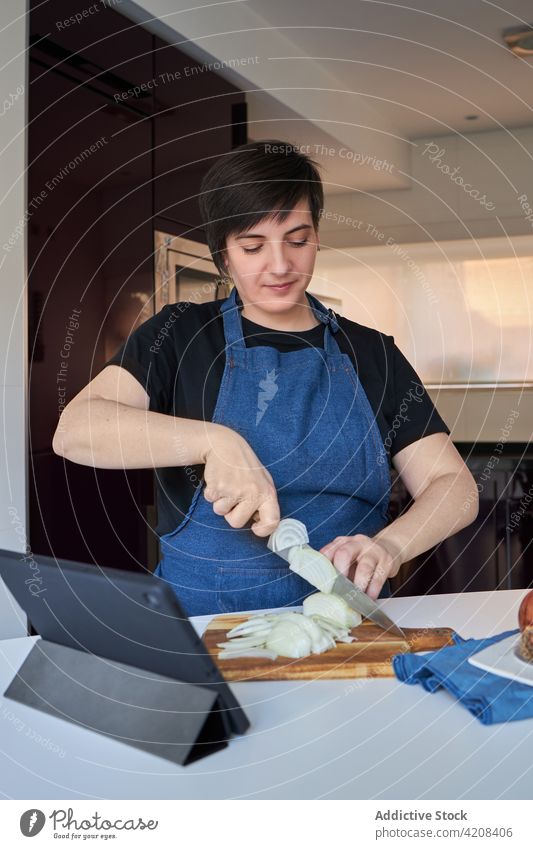 Glückliche Hausfrau beim Zwiebelschneiden in der Küche Frau geschnitten Koch heimwärts Lächeln organisch roh Schürze heiter kulinarisch frisch Schneidebrett