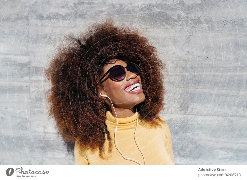 Frohe trendige schwarze Frau lachend auf grauem Hintergrund heiter Afro-Look Frisur charmant genießen farbenfroh Porträt Inhalt Glück hell Lächeln sanft Angebot