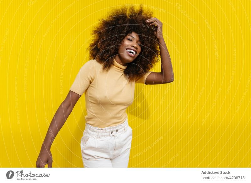 Frohe trendige schwarze Frau lachend auf gelbem Hintergrund heiter Haare berühren Afro-Look Frisur charmant genießen offen farbenfroh Porträt Inhalt Glück hell