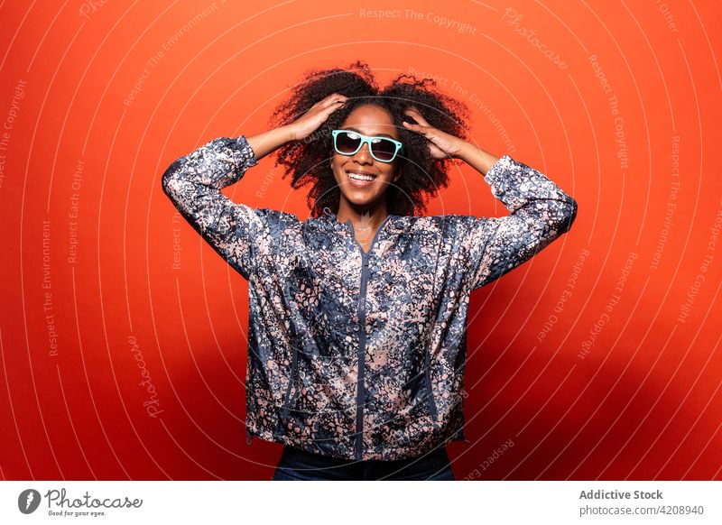 Stilvolle schwarze Frau mit Sonnenbrille vor rotem Hintergrund selbstbewusst cool Outfit Vorschein unabhängig Glück Windstille trendy Lächeln Streetstyle
