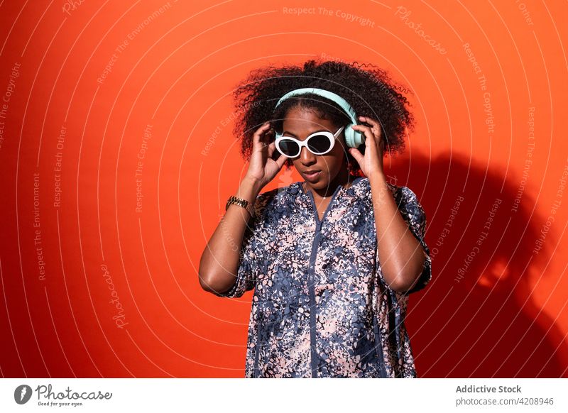Glückliche schwarze Frau, die mit Kopfhörern gute Musik hört zuhören Arme hochgezogen konzentriert unterhalten Gesang meloman Melodie Klang cool Audio Outfit