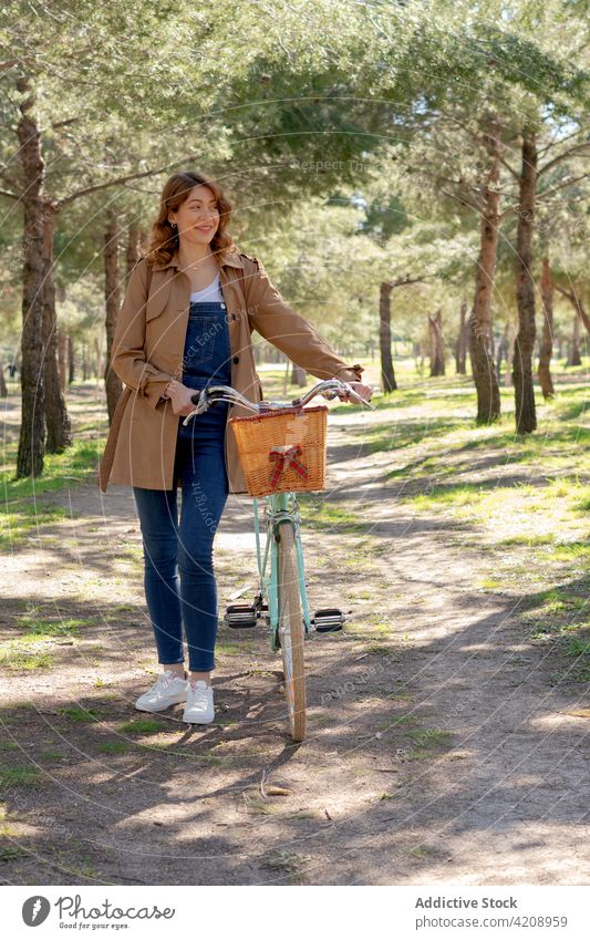 Glückliche junge Frau in der Nähe von Fahrrad auf unbefestigtem Weg Lächeln heiter Schmutz Straße Park Hobby positiv Inhalt Aktivität froh Stil Nutzholz Weide